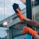 Young female worker cleaning window glass with cloth in spacious villa